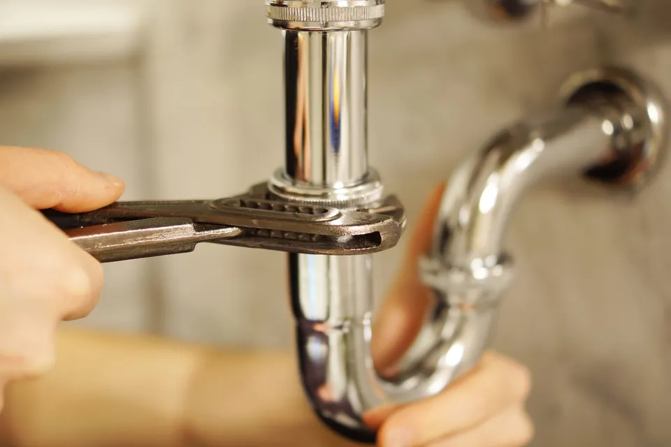 Gros plan sur une pince multiprise serrant la bague d’un siphon chromé sous un lavabo