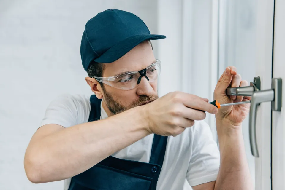Technicien en lunettes de protection reprenant la fixation d’une poignée sur une menuiserie blanche